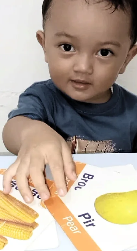 Seorang anak laki-laki DaycareQu berkaus biru meraih kartu bergambar di meja.