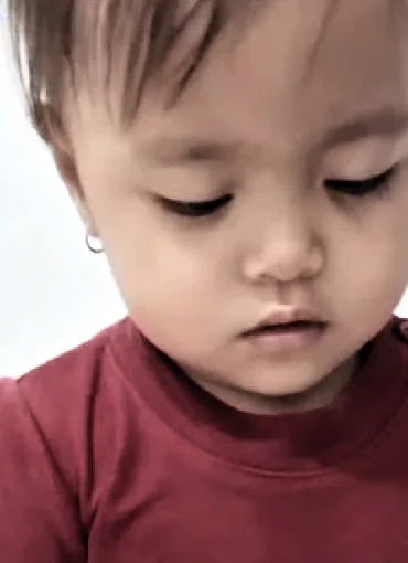 Seorang anak perempuan DaycareQu berkaus merah memegang sebuah kartu dan menunduk mengamatinya.