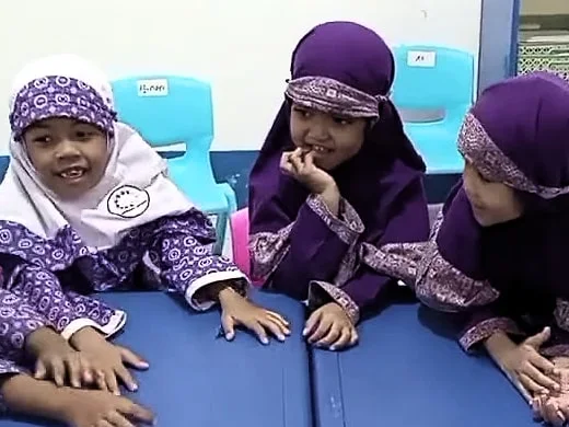 Anak-anak RA berseragam ungu tertawa sambil bersandar di meja biru.
